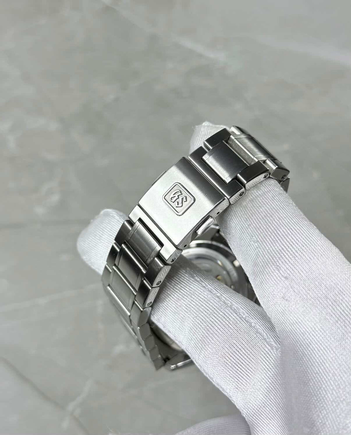 Grand Seiko White Birch close-up of the GS-logo clasp and bracelet in a white glove.