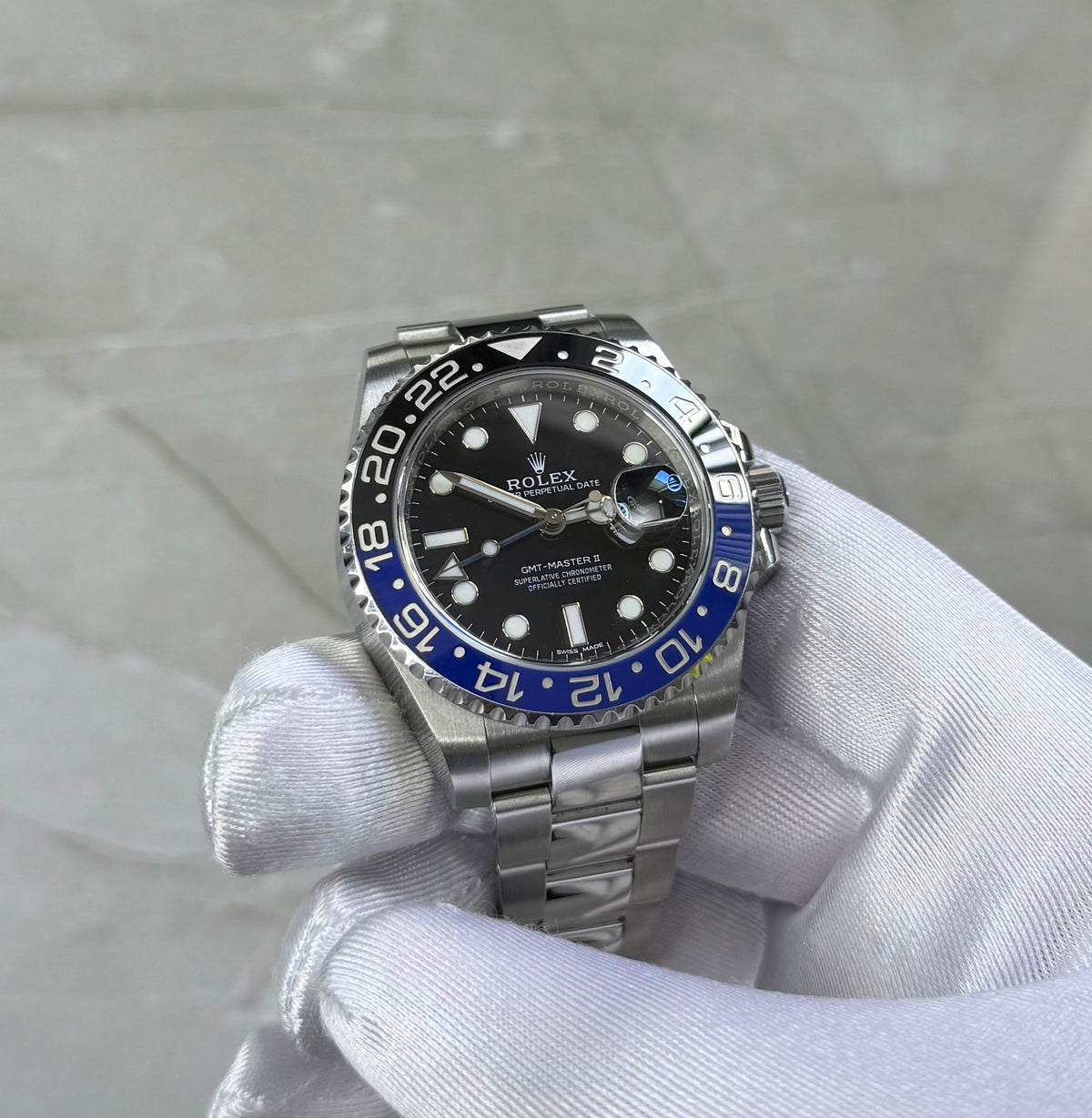 Rolex GMT-Master II Batman held face-on in a white glove showing black dial and blue-and-black bezel.