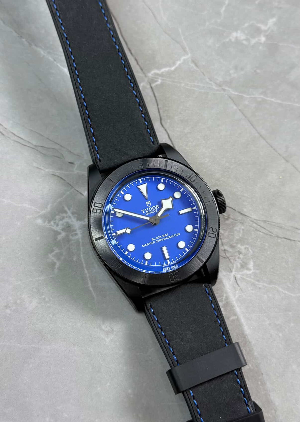 Tudor Black Bay Ceramic lying flat with blue dial, dark bezel and black strap with blue stitching.