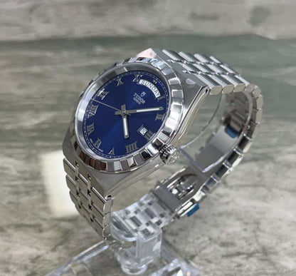 Tudor Royal Day Date crown-side angled view on a clear stand showing blue dial and bracelet loop.