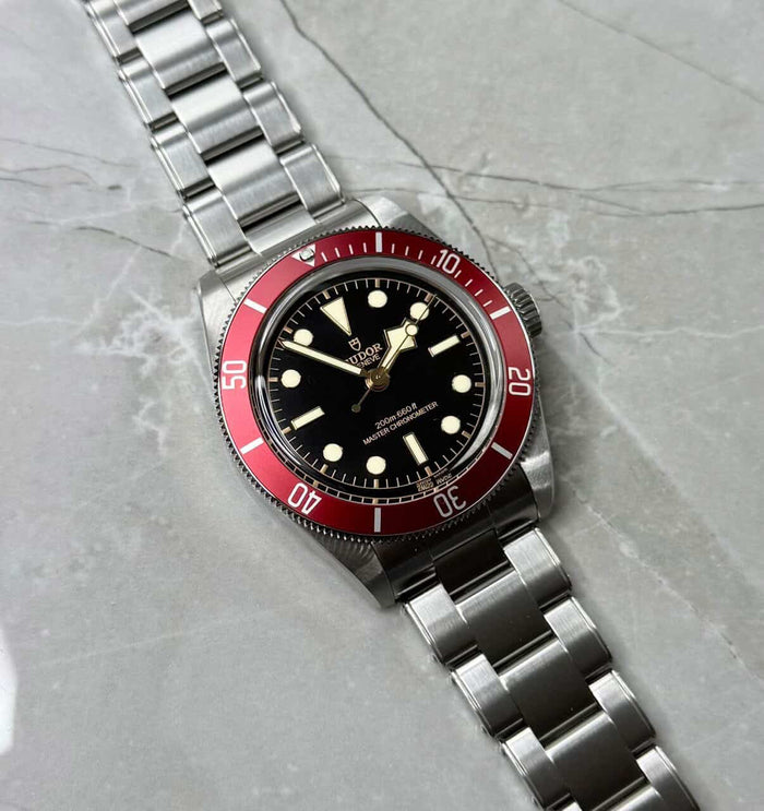 Tudor Black Bay Burgundy lying flat with black dial, burgundy bezel and three-link bracelet.