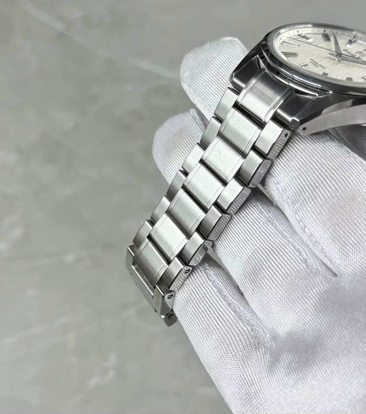 Grand Seiko White Birch angled bracelet view in a white glove with white dial partly visible.