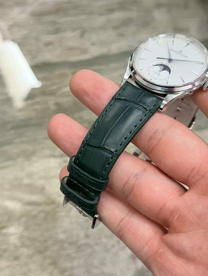 Jaeger-LeCoultre Master Ultra Thin Moon held at an angle showing the pale dial, moonphase display and dark textured strap with keepers.