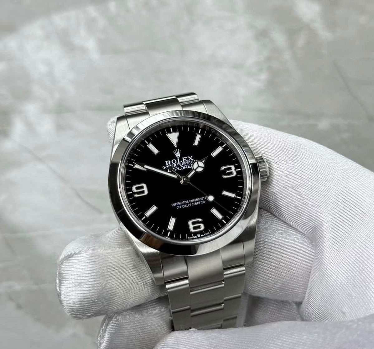 Rolex Explorer 40 held face-on in a white glove, showing the black dial, 3, 6 and 9 numerals and smooth bezel.