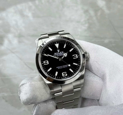 Rolex Explorer 40 held face-on in a white glove, showing the black dial, 3, 6 and 9 numerals and smooth bezel.