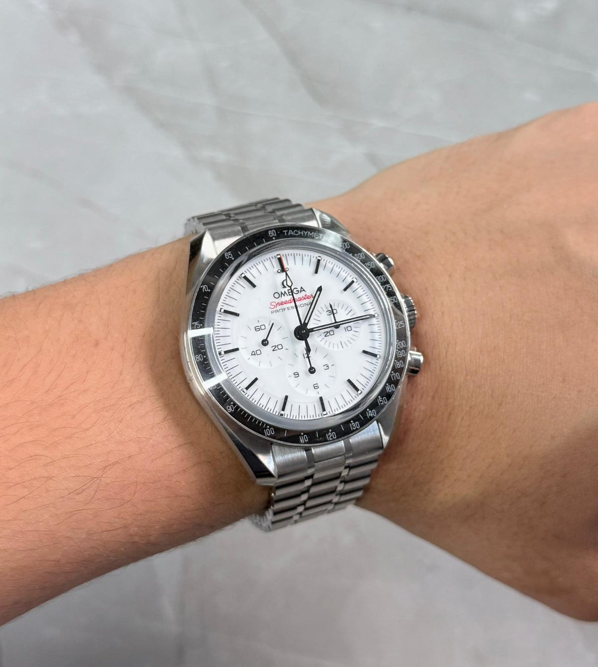 Omega Speedmaster on wrist with white chronograph dial and silver-tone bracelet.