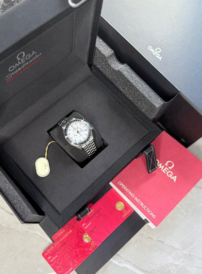 Omega Speedmaster displayed in an open black presentation box with white dial, tag, red cards and printed booklet.