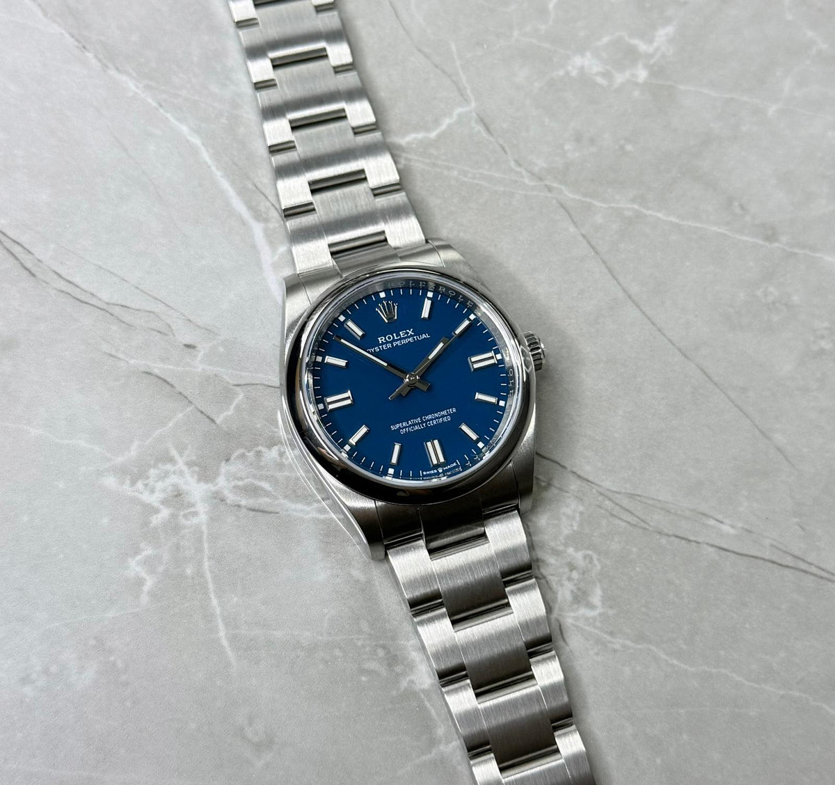 Rolex Oyster Perpetual 36 lying flat with blue baton-marker dial, smooth bezel and three-link bracelet.
