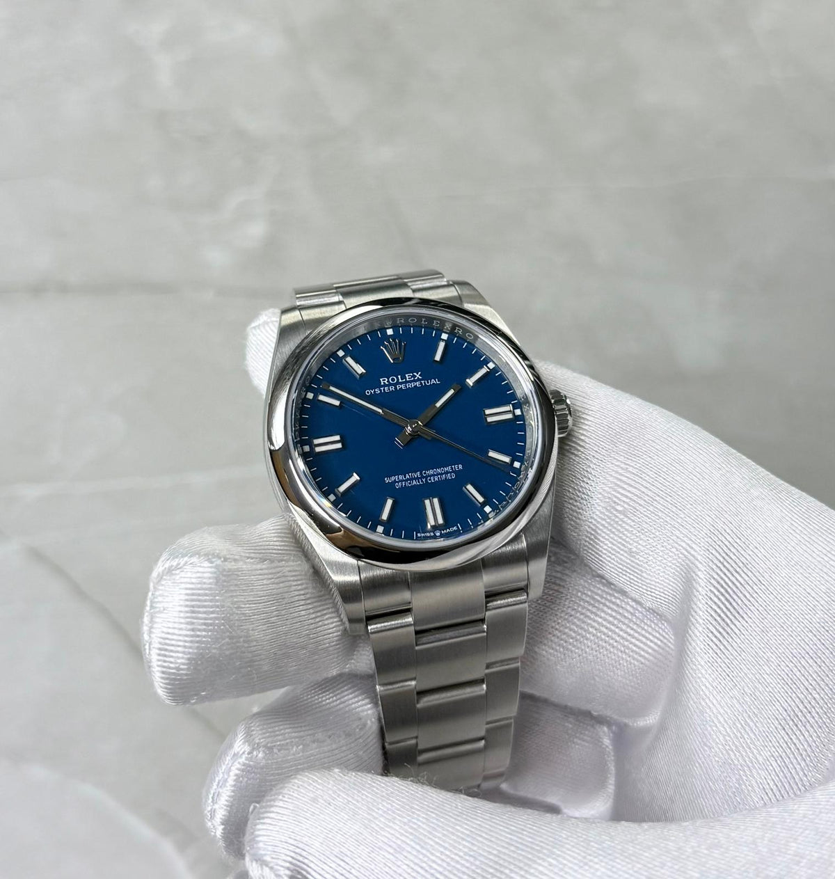 Rolex Oyster Perpetual 36 held face-on in a white glove showing blue dial and baton hour markers.