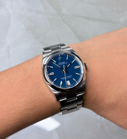 Rolex Oyster Perpetual 36 on wrist with blue dial and three-link bracelet.