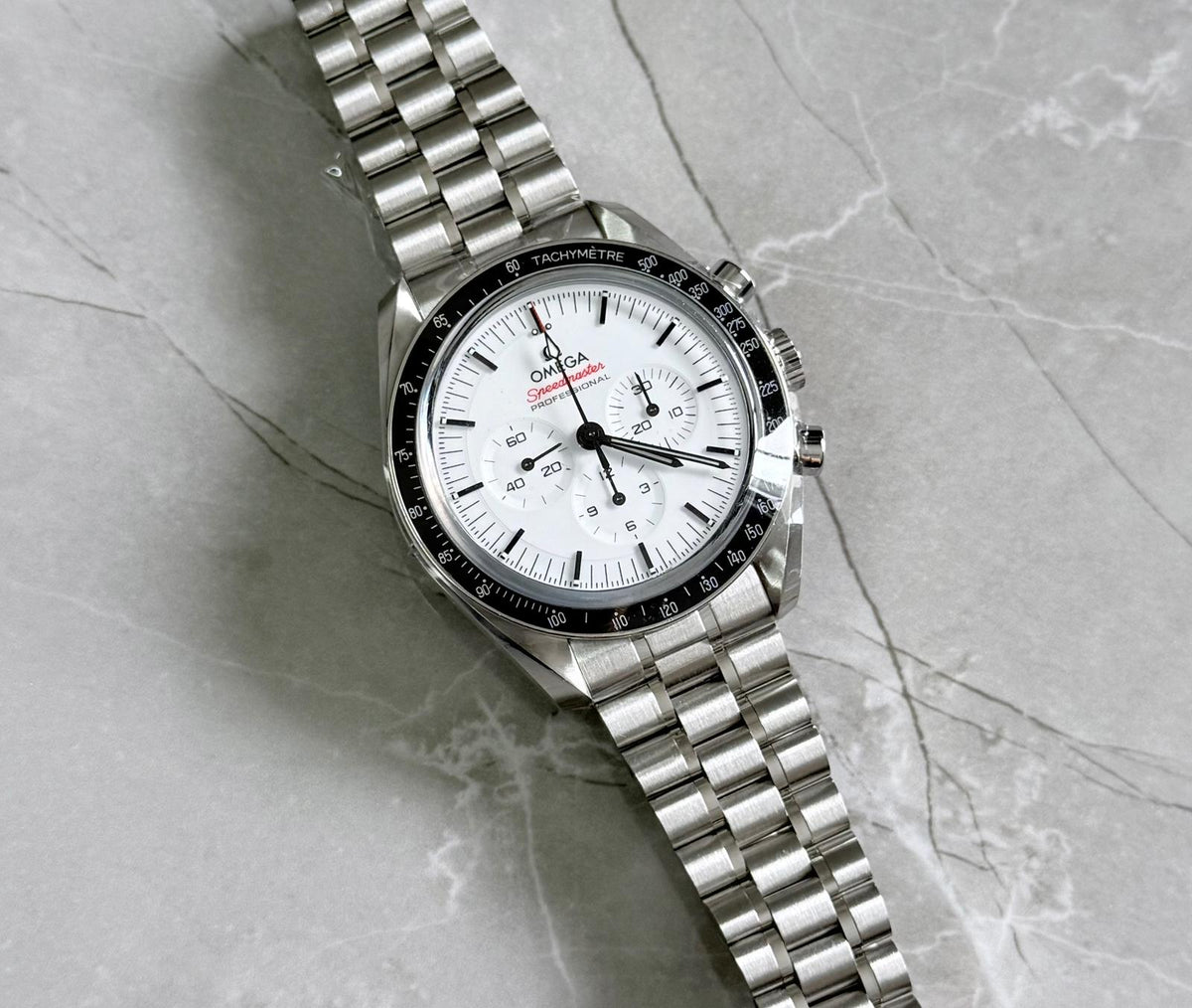 Omega Speedmaster lying flat with white chronograph dial, black tachymeter bezel and bracelet.