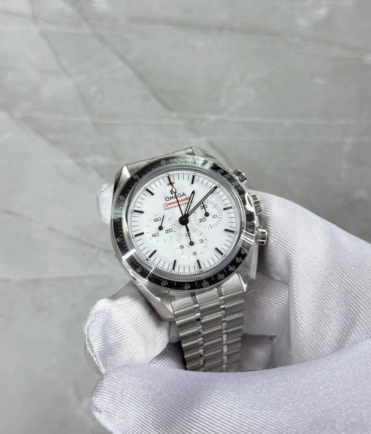 Omega Speedmaster held in a white glove showing white dial, three subdials and black bezel.
