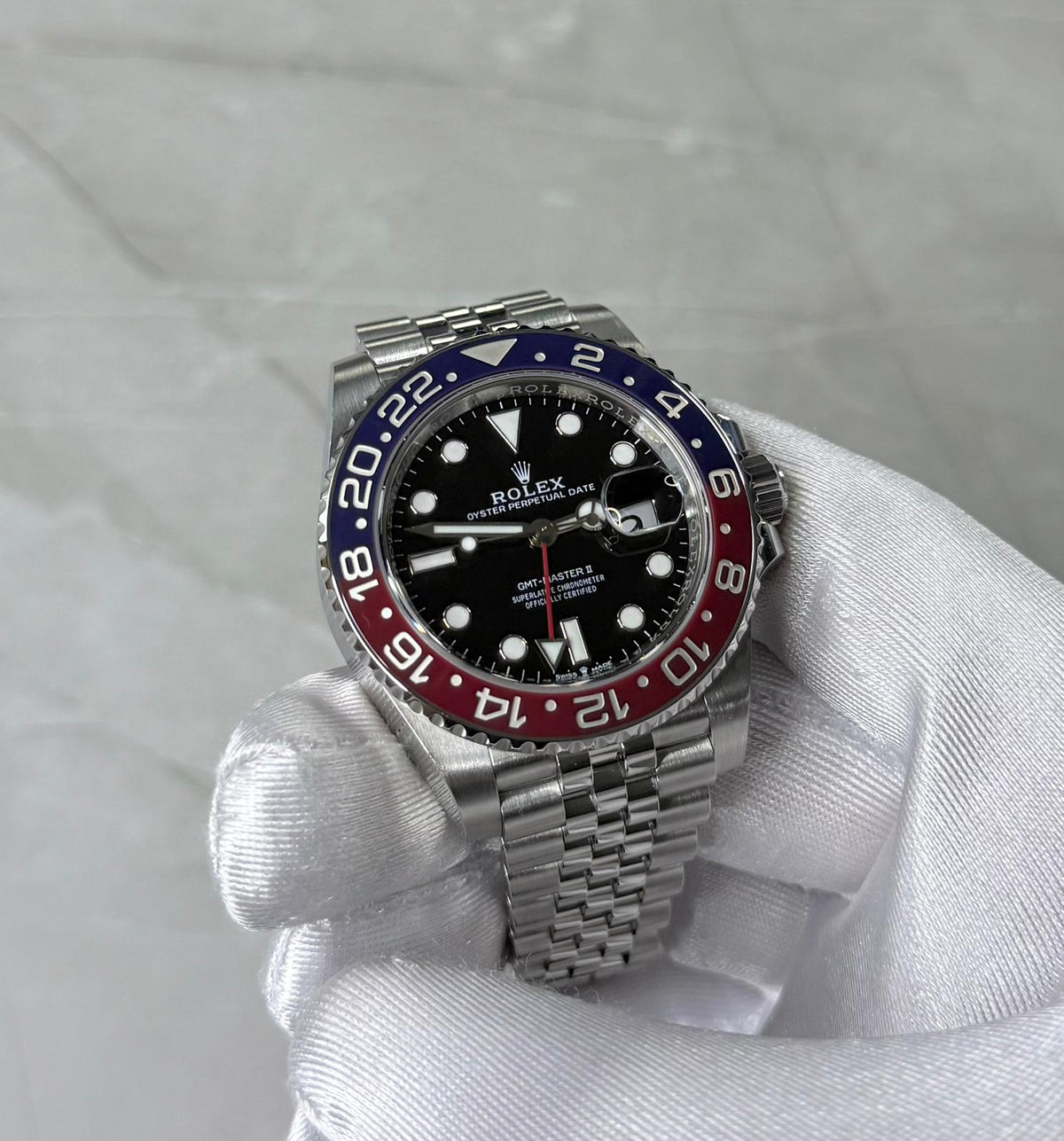 Rolex GMT-Master II Pepsi held in a white glove showing black dial and red-and-blue 24-hour bezel.