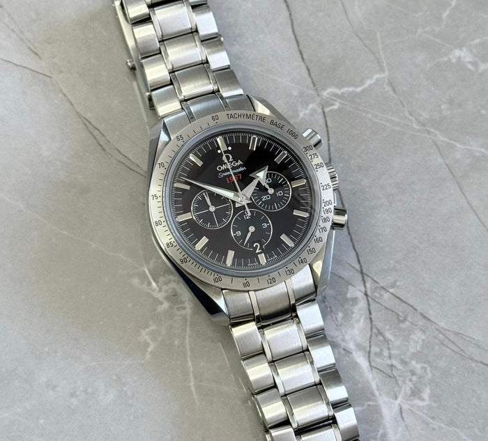 Omega Speedmaster Broad Arrow lying flat with black chronograph dial and silver-tone tachymeter bezel.