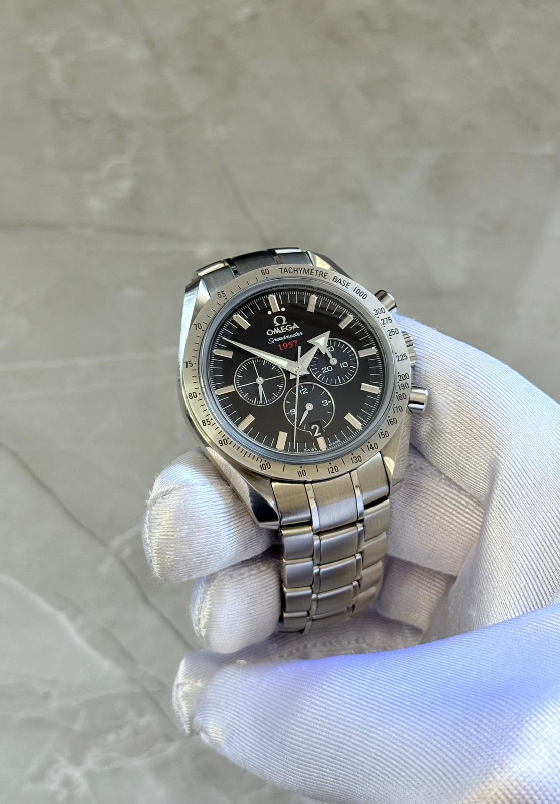 Omega Speedmaster Broad Arrow held in a white glove showing black dial, broad-arrow hand and three subdials.
