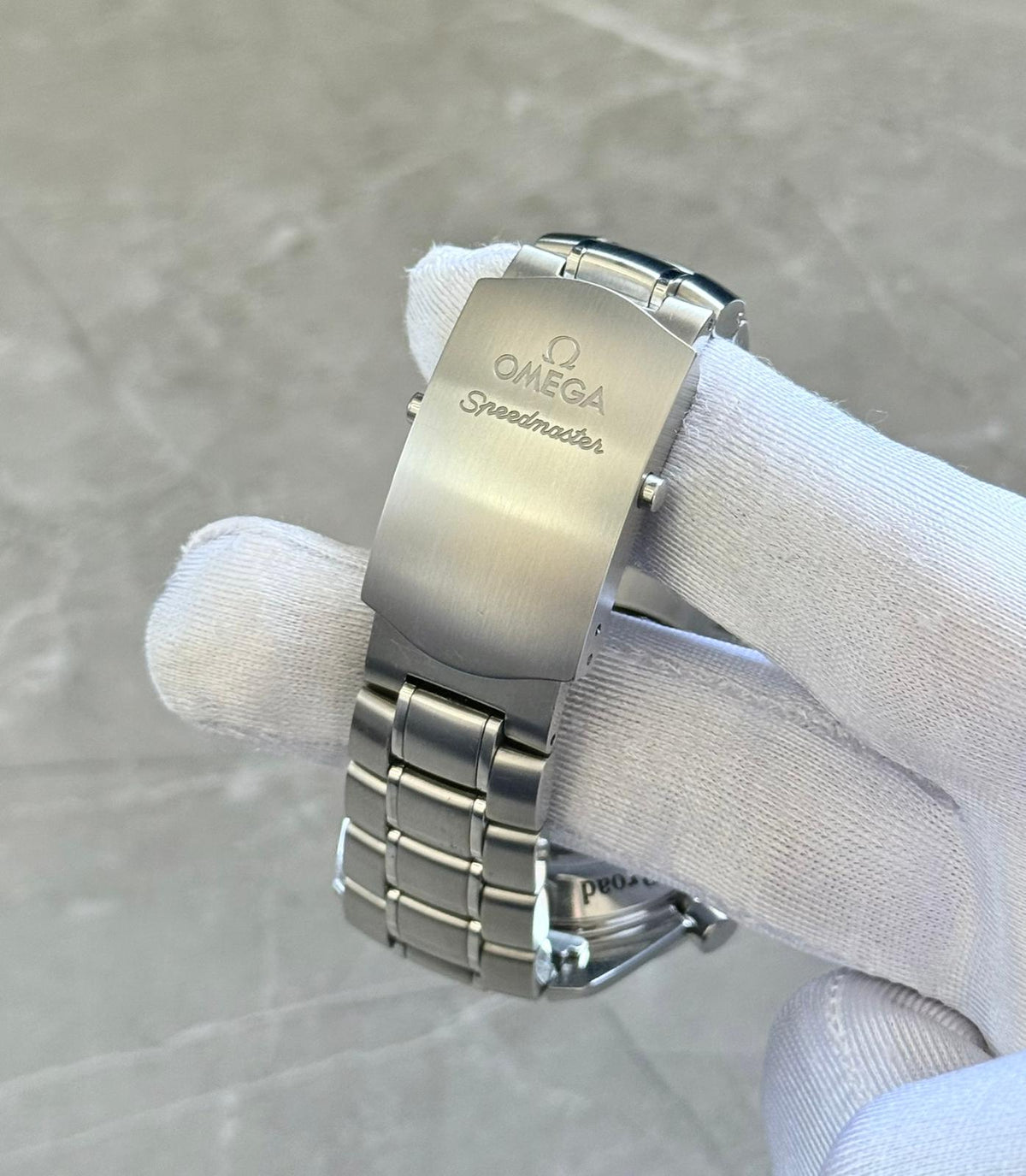 Omega Speedmaster Broad Arrow close-up of the Omega Speedmaster-branded folding clasp in a white glove.