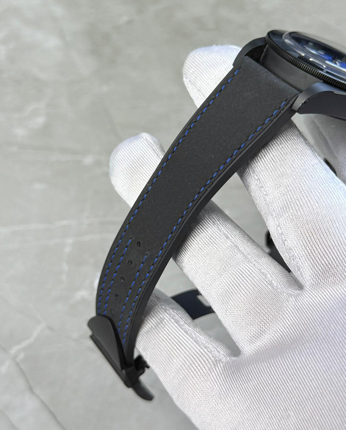 Tudor Black Bay Ceramic angled strap view in a white glove showing blue stitching and case edge.