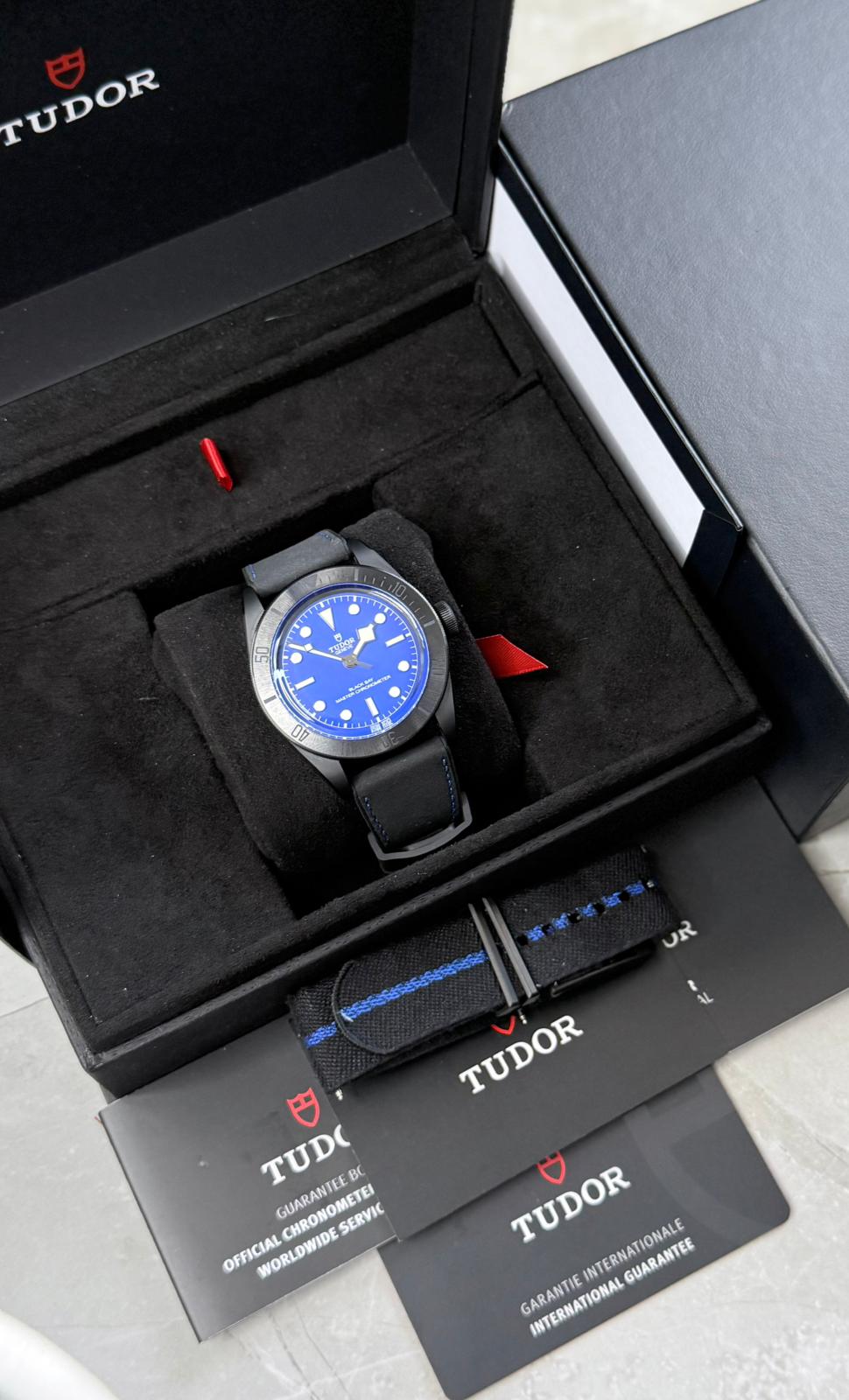 Tudor Black Bay Ceramic displayed in an open black box with blue dial, extra strap and printed booklets.